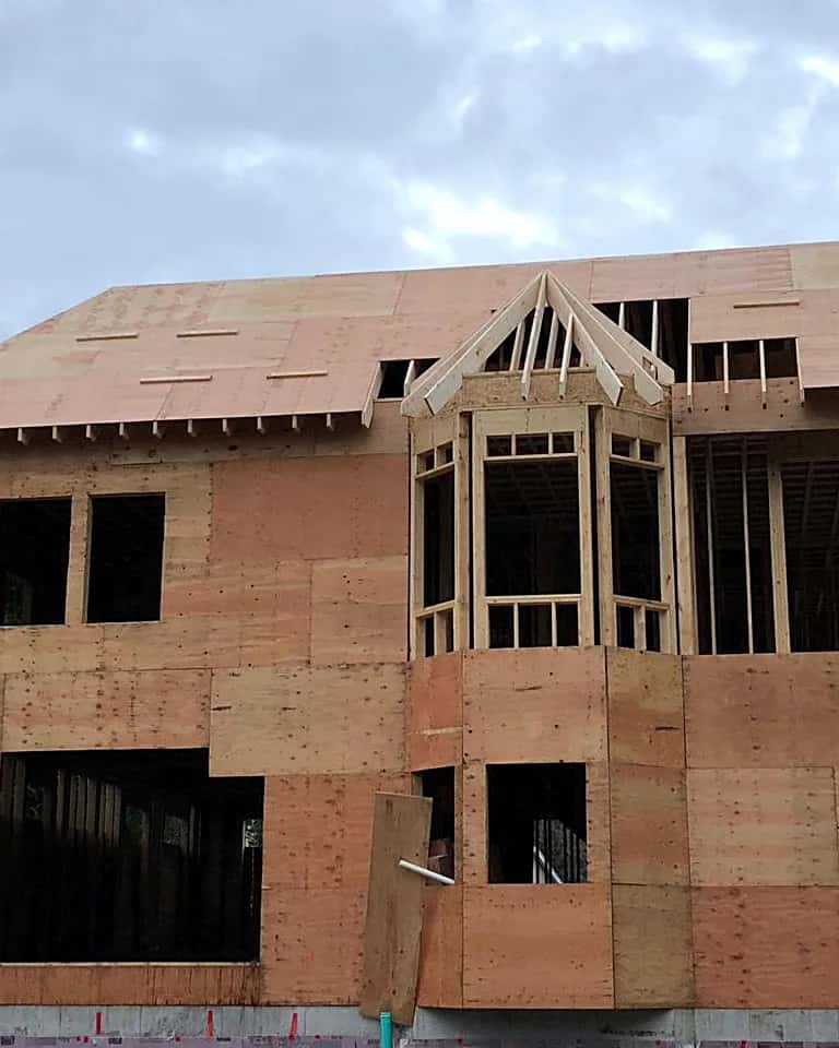 Two-story wood-frame house with a bay window, sheathed and awaiting siding