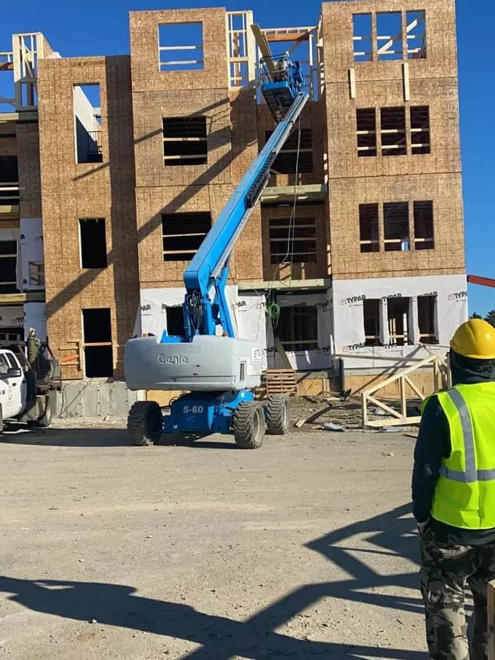 Multi-story wood-frame residential building under construction, with a boom lift on site